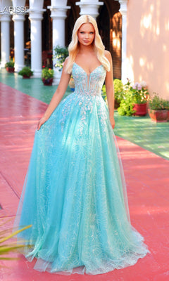 A woman in a seafoam Clarisse Designs 62310 long prom dress with a corset bodice stands outdoors on a red and green walkway near potted plants and white columns.