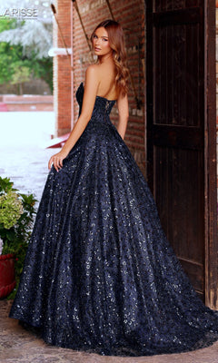 A woman stands in a doorway wearing the Long Prom Dress: Clarisse Designs 62326, a dark navy strapless gown with a full skirt and subtle patterned texture, elegantly looking over her shoulder.