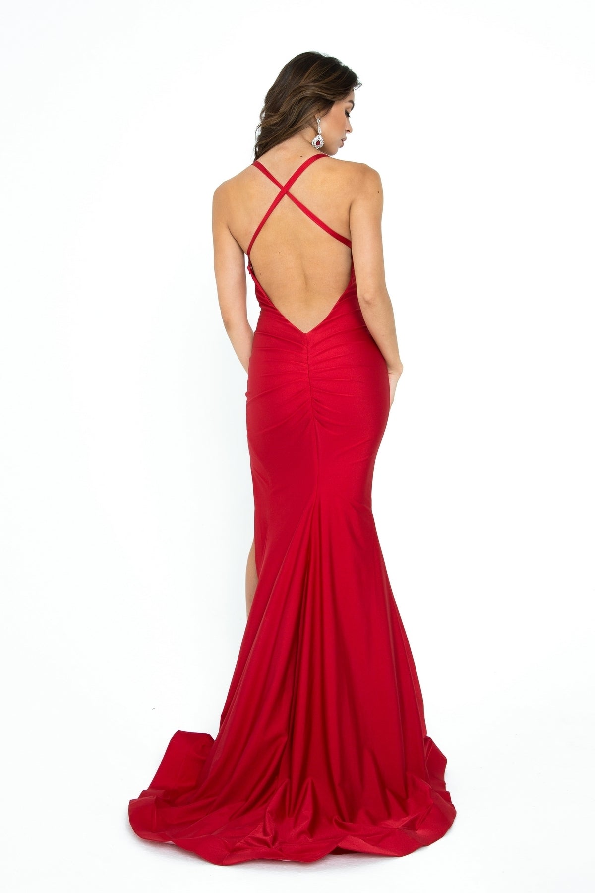 A woman models the Atria 6308H Strappy-Back Long V-Neck Prom Dress, featuring a fitted silhouette, crisscross straps, v-neckline, and low open back, against a white background.