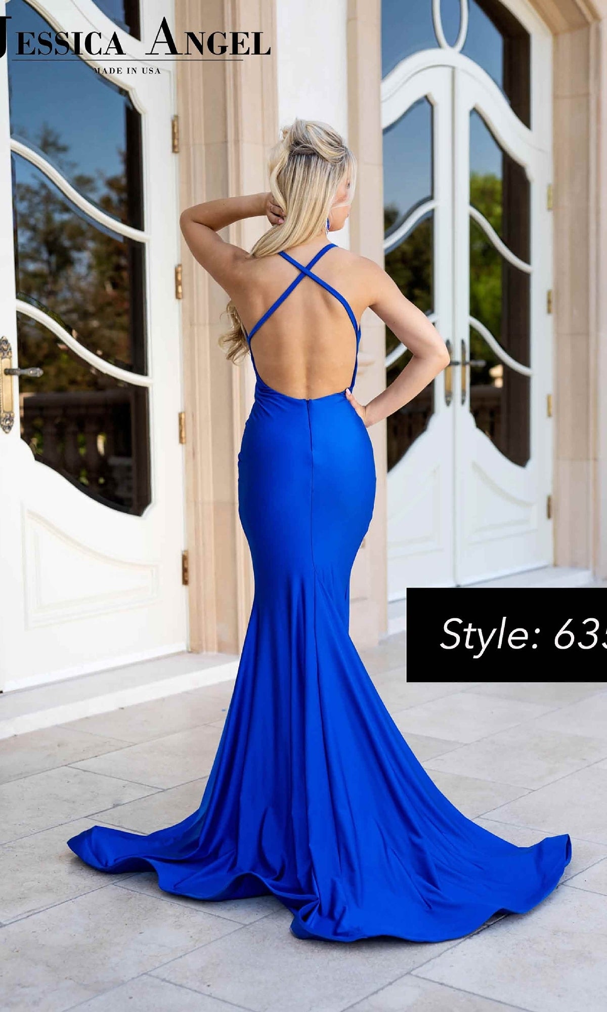 Woman in a vibrant blue, floor-length Jessica Angel 635 Strappy-Back Long Prom Dress with a mermaid skirt and crisscross backless straps, standing outside in front of white double doors.