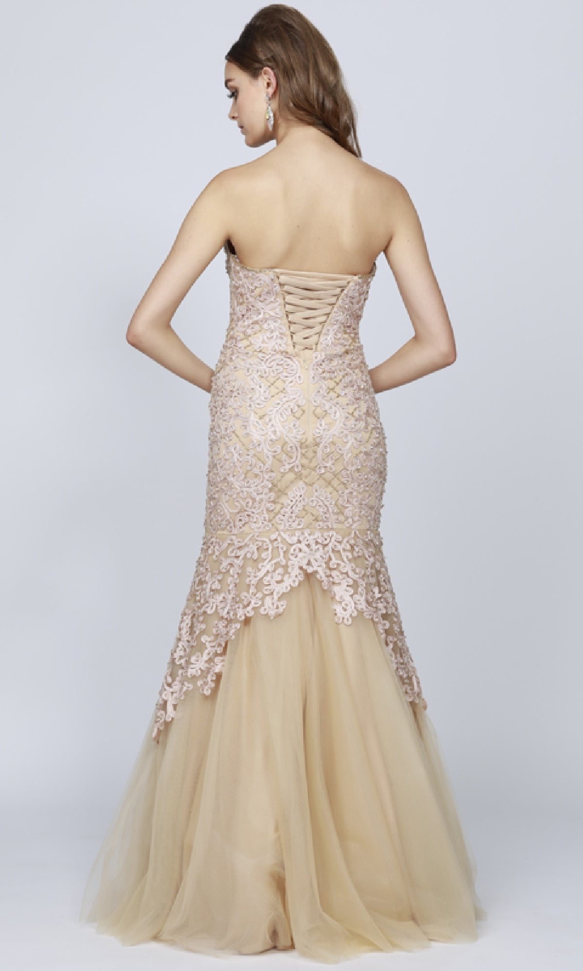 A woman wearing the Juliet 644 Long Mermaid Prom Dress—strapless, floor-length beige with lace details and a lace-up back—stands against a plain light background, ideal for prom or formal events.