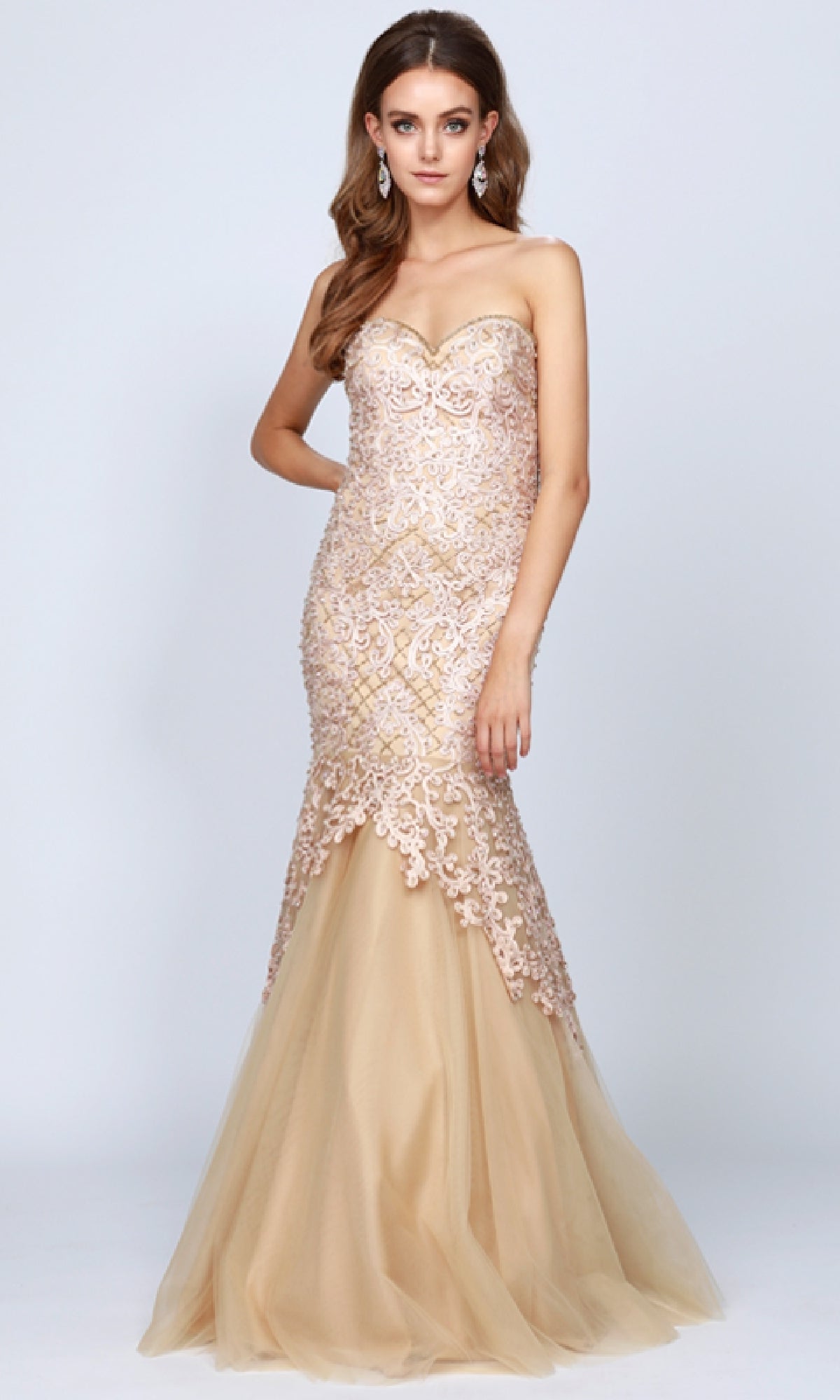 A woman wears the Juliet 644 Long Mermaid Prom Dress, featuring a strapless lace bodice and champagne tulle skirt—an elegant choice for formal events—while standing against a plain background.