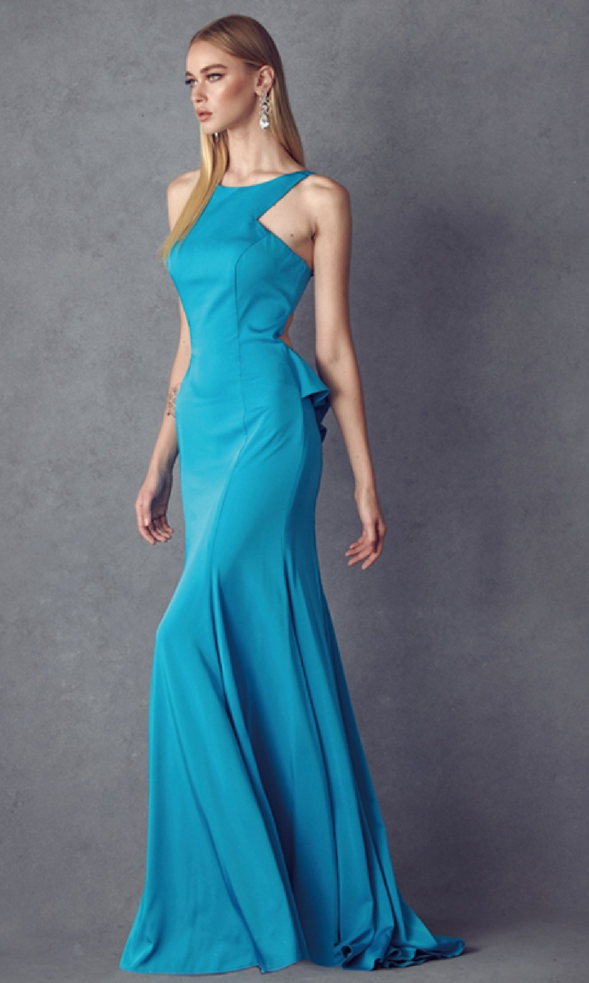 A woman models the Juliet 645, a sleeveless, floor-length turquoise prom dress with racer front and side cutouts, against a plain grey background.