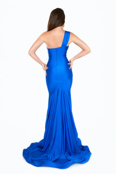 A woman faces away from the camera in a royal blue Atria 6528H prom dress, featuring a fitted one-shoulder design, dramatic mermaid skirt, floor-length hem, and long train.