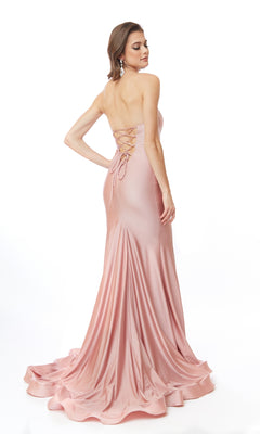 A woman stands against a white background, looking over her shoulder in the Atria 6544H Lace-Up Strapless Long Prom Dress—a floor-length pink satin gown with a lace-up back.