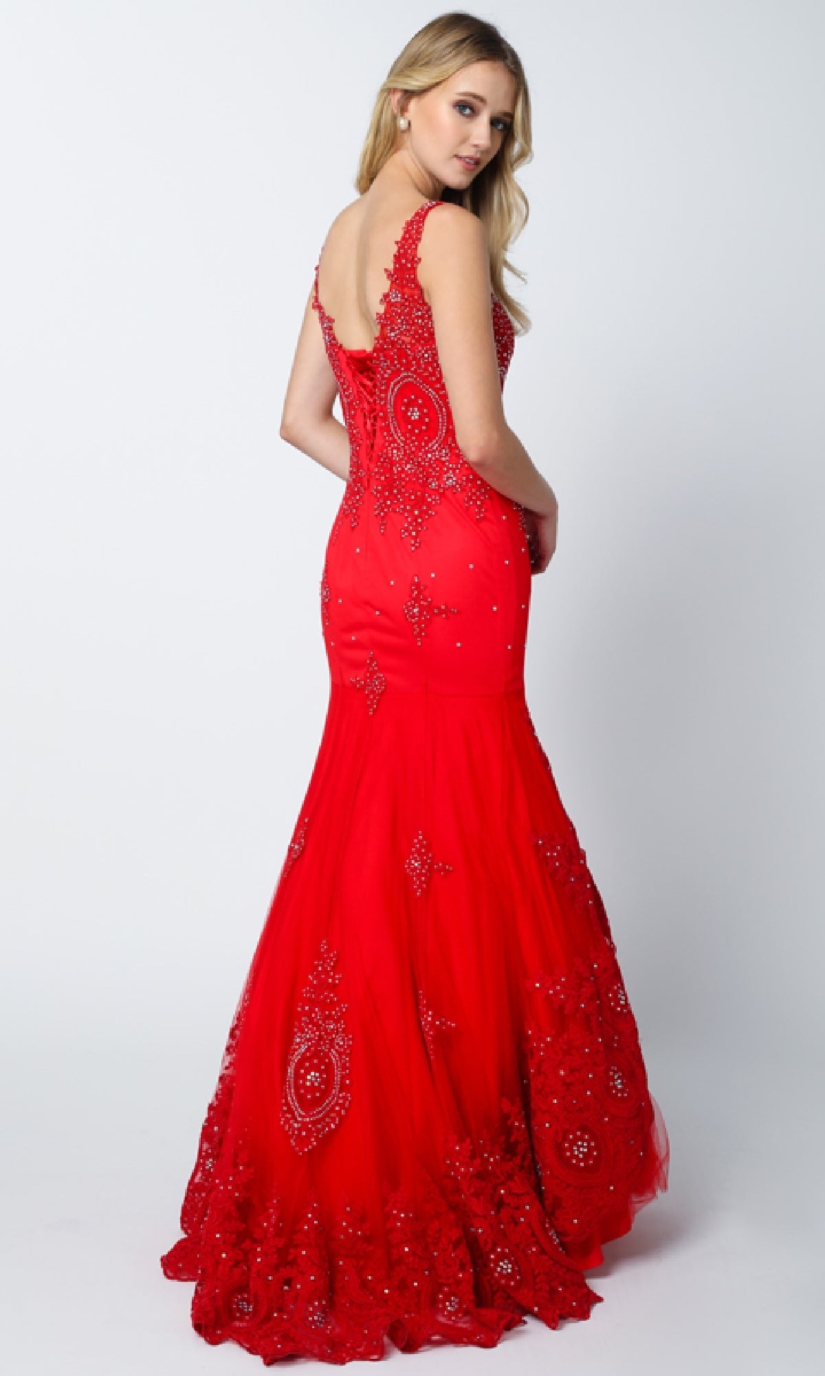 A woman with long blonde hair wears the Juliet 654 long prom dress, a fitted red mermaid gown with beaded embellishments, posing over her shoulder against a plain white background.