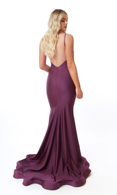 A woman with long blonde hair models the Atria 6566H Backless Long V-Neck Prom Dress, a floor-length purple gown with a mermaid skirt and small train, standing against a white background.