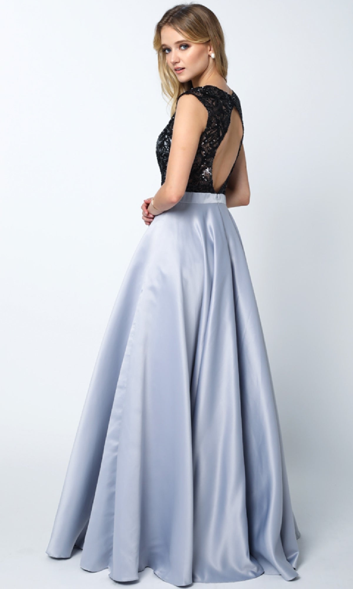 Woman modeling the Juliet 661 Cut-Out Long A-Line Prom Dress, featuring a black lace open-back top and light gray satin skirt, standing and glancing over her shoulder.