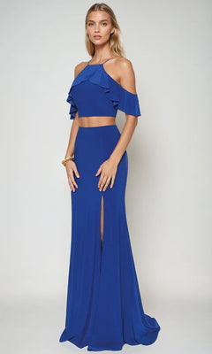 A woman wearing the Juliet 662 long prom dress—a royal blue two-piece with a cold-shoulder ruffled crop top and a high-waisted, floor-length skirt featuring a bold leg slit.