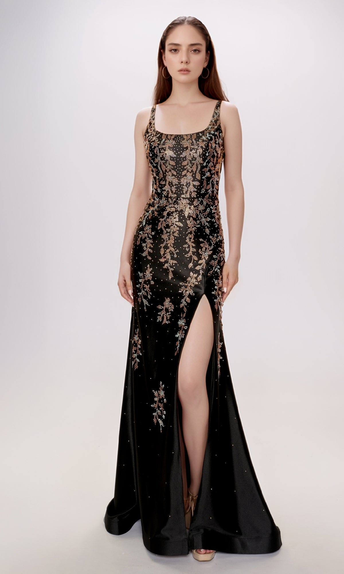 A woman stands against a plain light background wearing the Nina Canacci 6633 long formal dress—a sleeveless black gown with a square neckline, gold floral embroidery, and a high thigh slit.