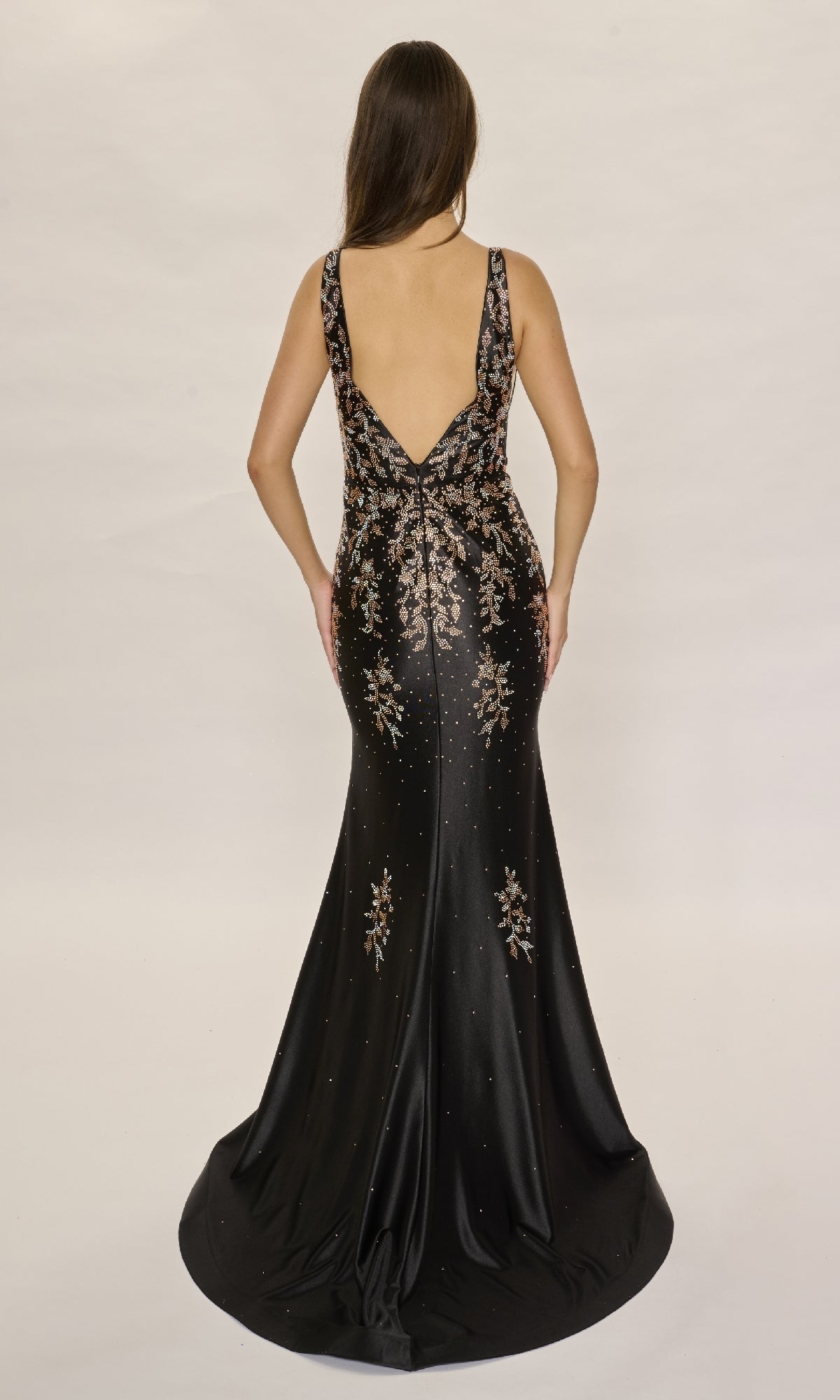 A woman wearing the Nina Canacci 6633 long formal dress, featuring metallic floral embellishments and rhinestone details, stands with her back to the camera against a plain background.