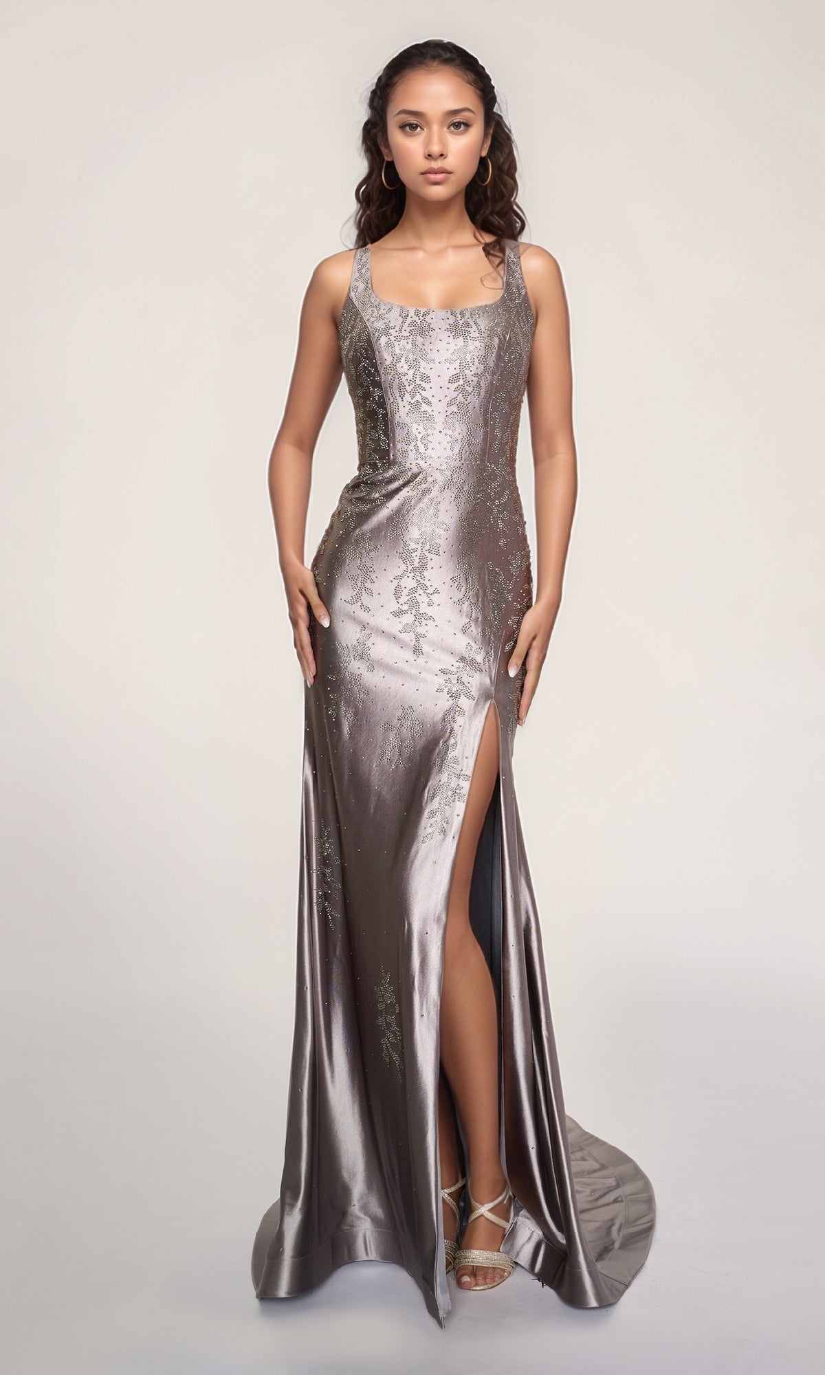 A woman wears the Nina Canacci 6633, a metallic silver, floor-length formal dress with a square neckline, high slit, and subtle floral patterns, paired with strappy heels against a plain light background.