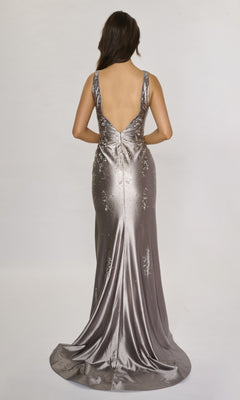 A woman faces away, wearing the Nina Canacci 6633—a metallic silver long formal dress with rhinestone details, a deep V-back, and a floor-length, slightly flared train.