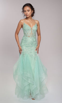 A woman wears the Nina Canacci 6637, a light green, sleeveless, floor-length formal dress with sheer and lace details and a lace-up open back, standing against a plain light background.