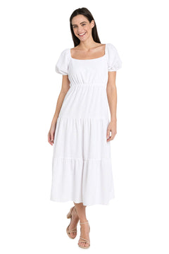 A woman in the Tea-Length White Party Dress: R&M Richards 6669, featuring short sleeves and a square neckline, pairs it with nude sandals while standing against a plain white background.