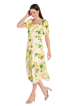 A woman smiles while standing in the Petite Midi Yellow Print Party Dress: R&M 6672P with puff sleeves and beige high-heeled sandals.