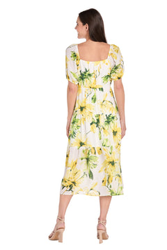 A woman faces away wearing the Sunflower Print Casual Dress: R&M Richards 6672, featuring white fabric with yellow sunflower details, short sleeves, a tiered midi skirt, and paired with nude heels for a chic casual look.