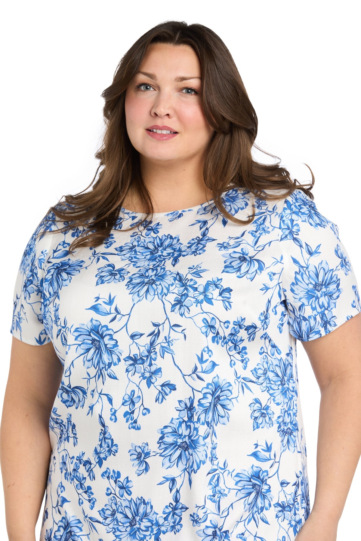 A woman with long brown hair models the R&M Richards 6674W plus-size short print party dress, featuring a white and blue floral pattern, against a plain white background.
