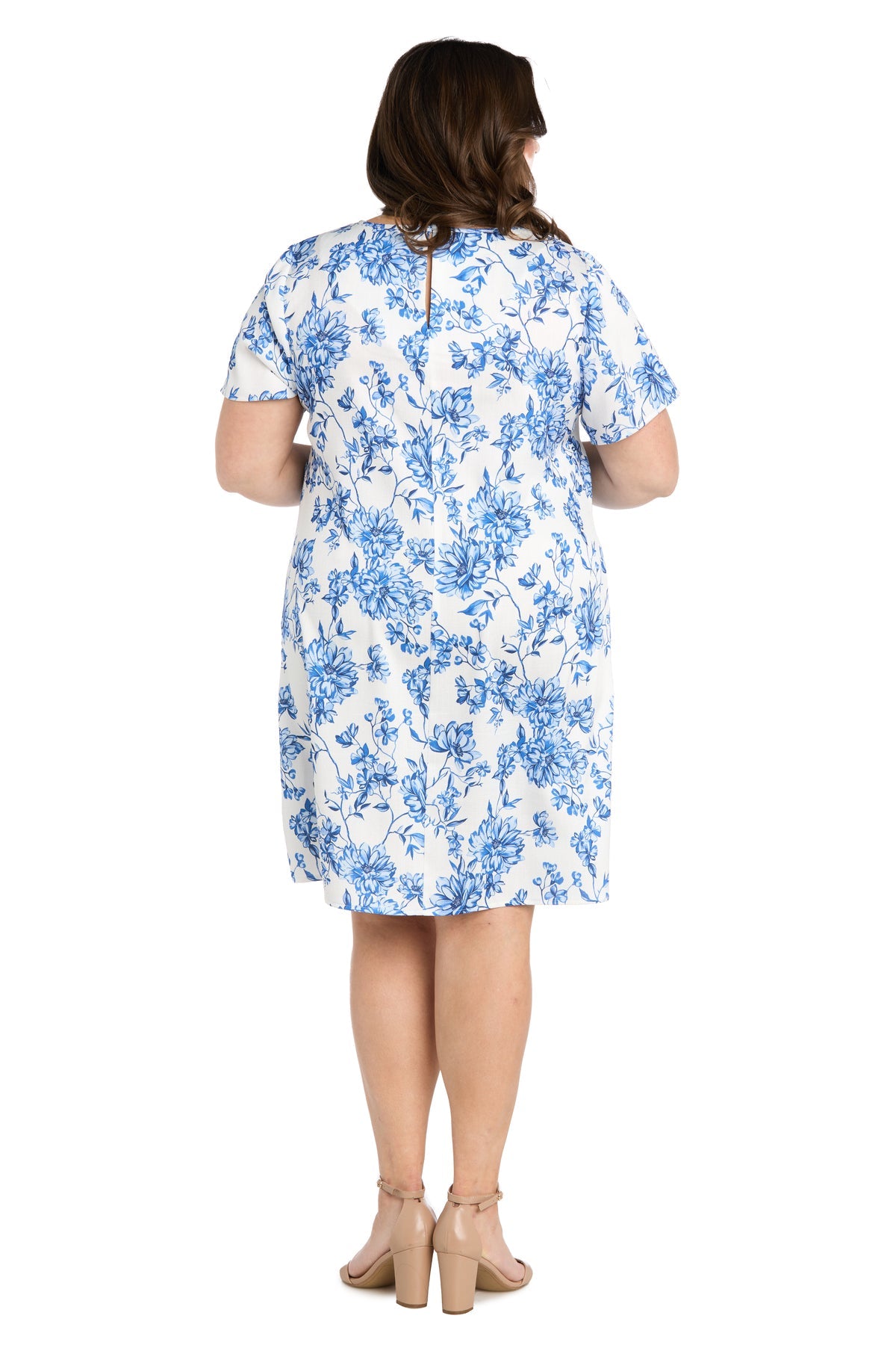 Woman standing with her back to the camera, wearing the R&M Richards 6674W Plus-Size Short Print Party Dress, featuring a white floral print with blue details and nude block-heeled shoes, against a plain white background.