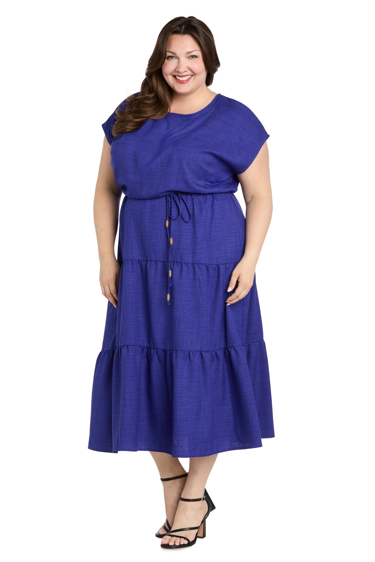 A woman smiles in black heeled sandals, wearing the R&M Richards 6680W Plus-Size Indigo Casual Dress—an ankle-length, short sleeve, tiered design with a drawstring waist—perfect for casual occasions.