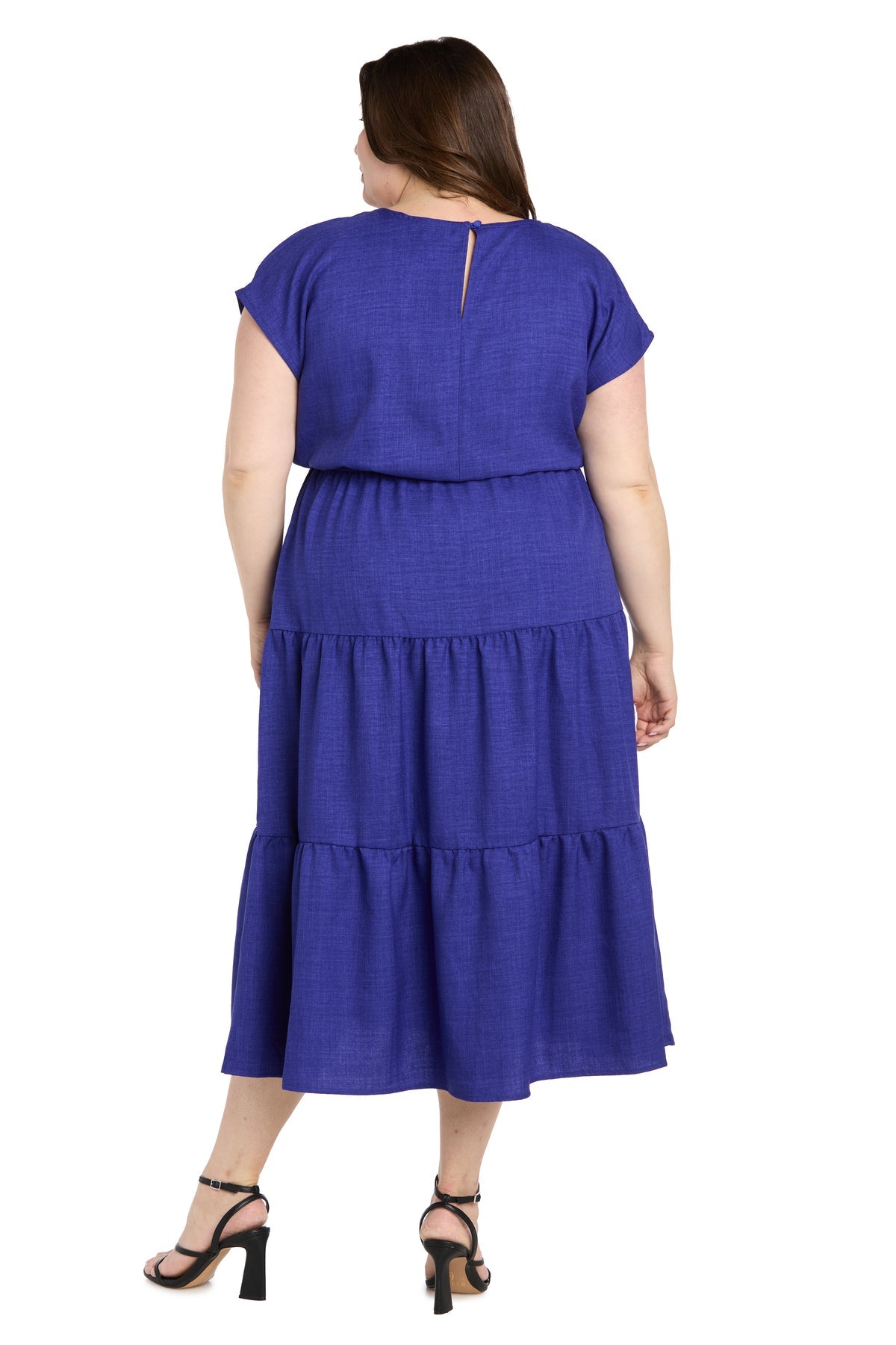A woman models the Plus-Size Indigo Casual Dress: R&M Richards 6680W, featuring short sleeves and ankle-length tiered design, styled with black heeled sandals and shown from the back against a white background.