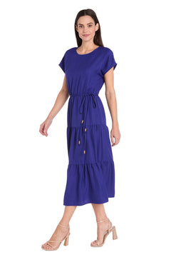 Woman wearing the R&M Richards 6680 Tea-Length Blue Party Dress with a waist tie and nude heeled sandals, standing against a white background.