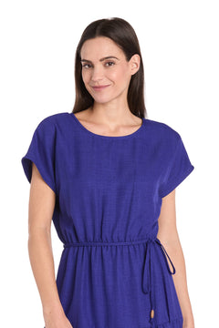 A woman with straight brown hair wears the R&M Richards 6680 Tea-Length Blue Party Dress with short sleeves and a belt, standing against a white background.