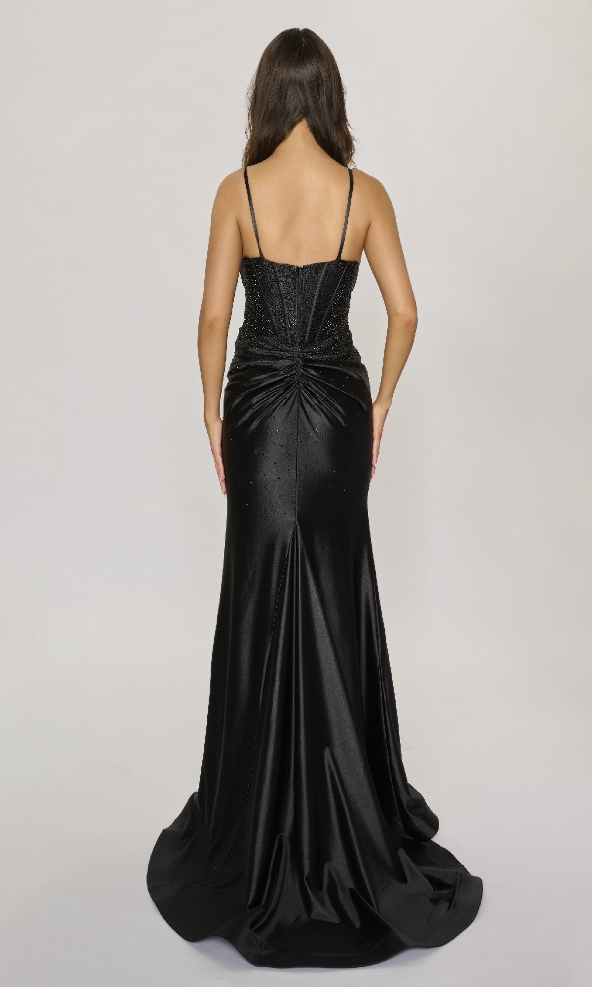 A woman with long brown hair is seen from behind wearing the Nina Canacci 6687—a black, floor-length formal dress featuring rhinestone embellishments—against a plain light background.