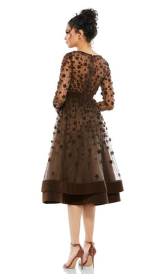 A woman stands with her back to the camera in the Mac Duggal 67007 knee-length wedding-guest dress featuring floral appliqués, sheer sleeves, and high heels.