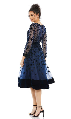 Woman wearing the Mac Duggal 67007 knee-length wedding-guest dress in navy blue with floral appliqué, beaded sheer long sleeves, and black high-heeled sandals, standing against a white background.
