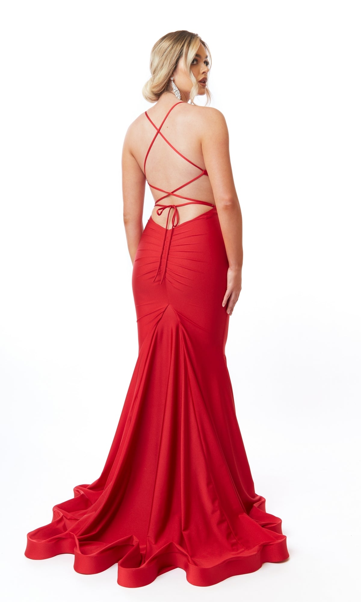 A woman faces away, wearing the Sexy Cut-Out Long Prom Dress: Atria 6703H—a floor-length red gown with an open back, crisscross straps, and a slight train—posing against a white background.