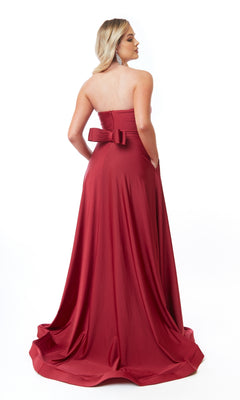 A person faces away, wearing the Strapless Sweetheart Long Prom Dress: Atria 6705H—an elegant red A-line gown with a back bow—set against a plain white background.