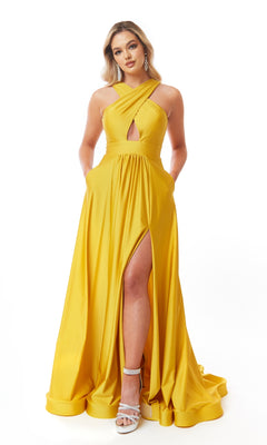Woman in the Atria 6706H Cut-Out Long A-Line Prom Dress, featuring a yellow floor-length design with a front slit and crisscross halter neckline, posing against a white background.