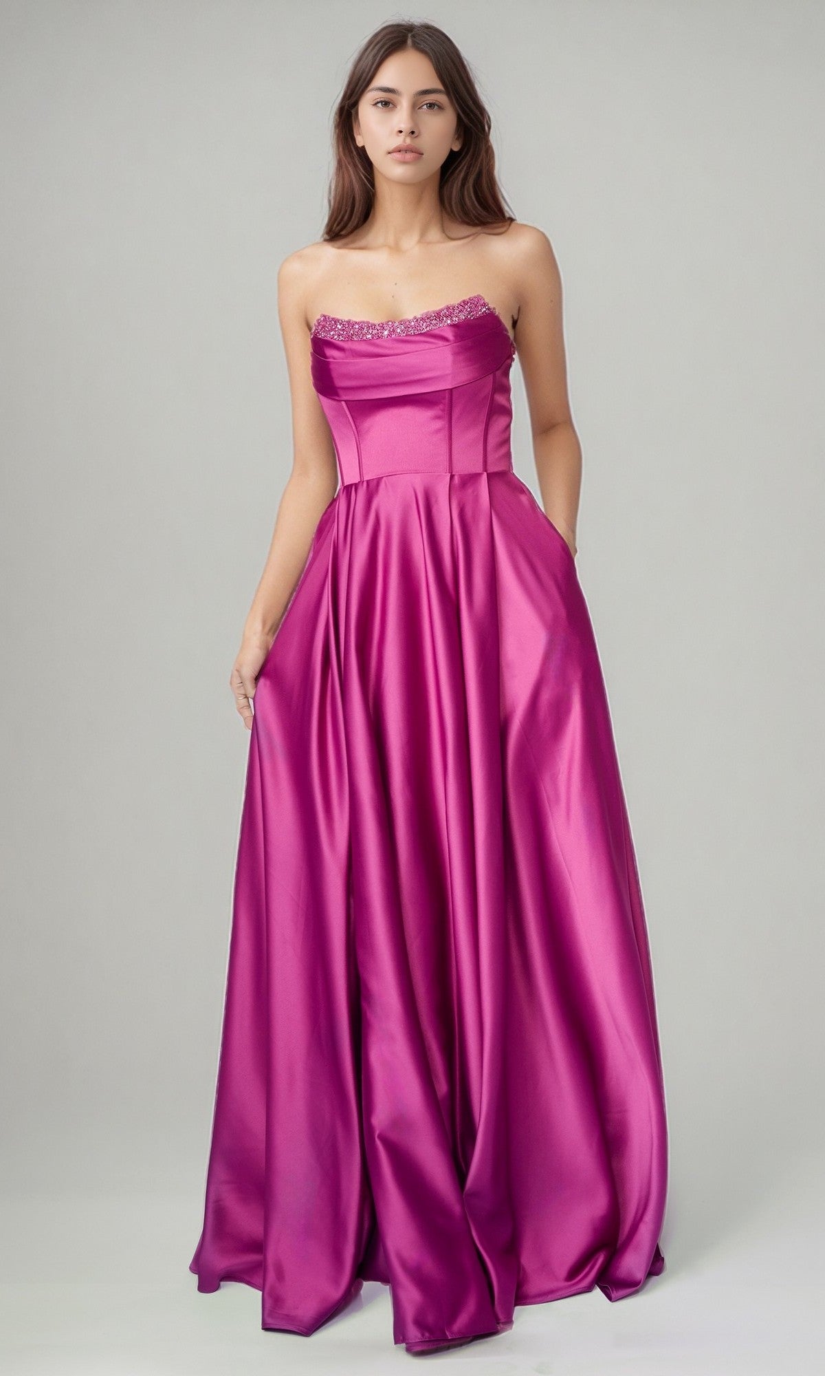 A woman models the Nina Canacci 6718 long formal dress—a magenta strapless satin gown with a fitted bodice and jeweled neckline—posing against a plain light gray backdrop.