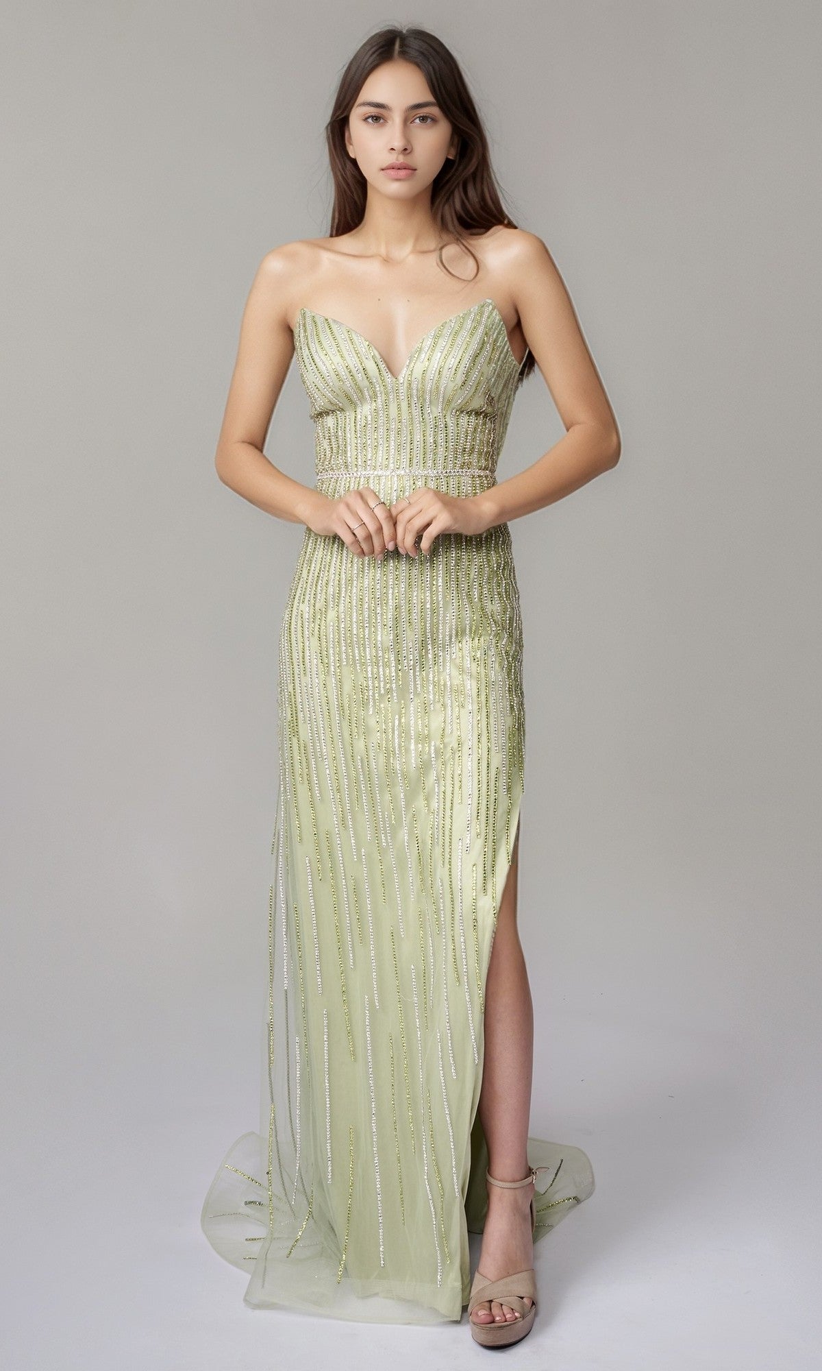 A woman poses against a plain background wearing the Nina Canacci 6723 long formal dress in pistachio—a strapless, floor-length gown with a high slit and sparkling linear beading.
