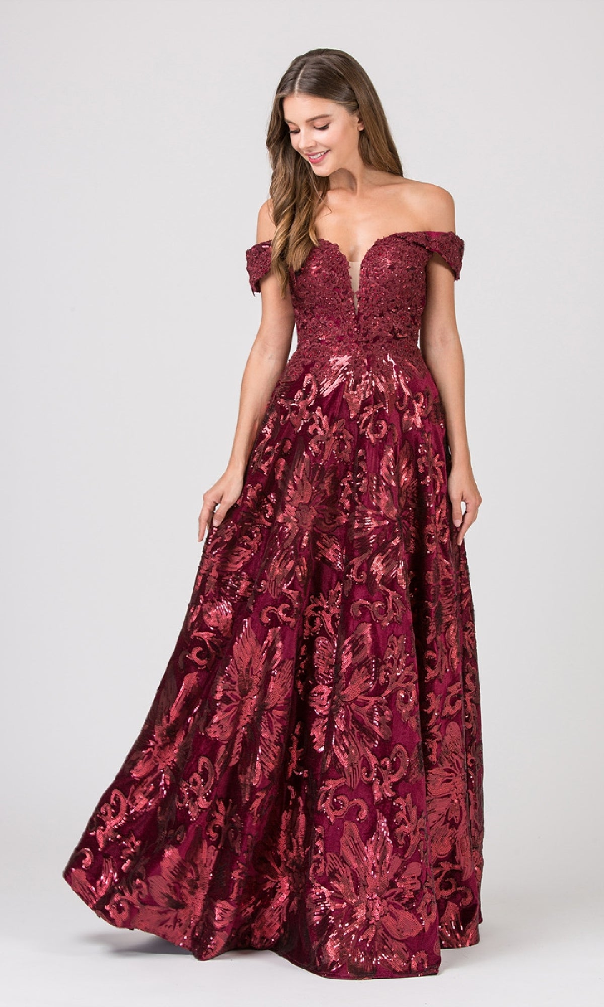 A woman stands against a plain background wearing the Eureka 6733 long formal dress, an off-the-shoulder, floor-length burgundy gown with an embellished bodice and sequined floral patterns.
