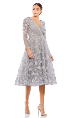 A woman in the Short Wedding Guest Dress 67387 by Mac Duggal, featuring floral appliqué details, long sleeves, and silver high heels, stands against a plain white background.
