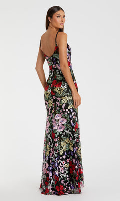 A woman stands against a plain white background, looking over her shoulder in the Mac Duggal 67473 Long Floral Formal Dress—a sleeveless, floor-length evening gown with an open back.