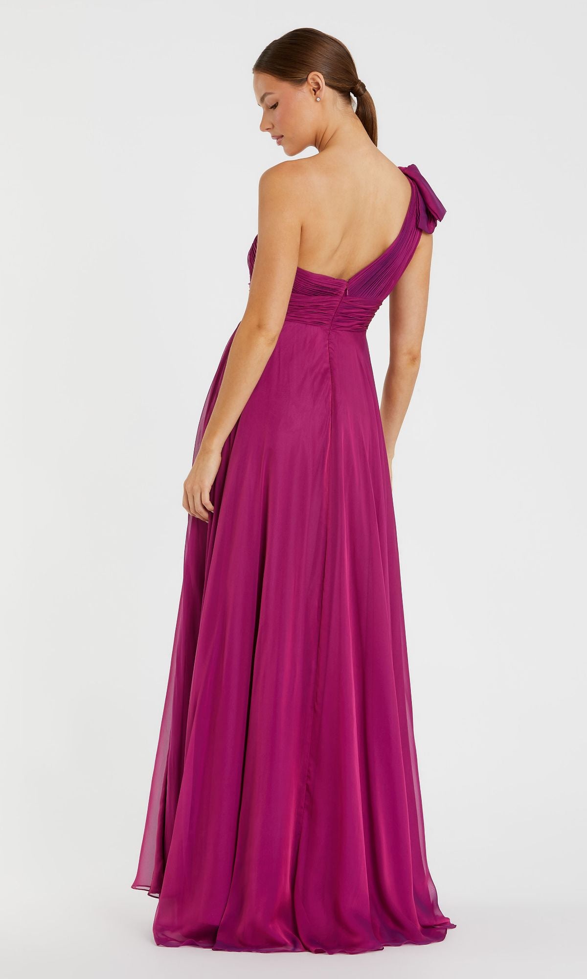 A woman stands facing away from the camera, wearing the Mac Duggal 67476—a floor-length magenta one-shoulder prom dress featuring a bow detail on the shoulder.