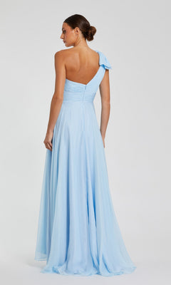 A woman stands with her back to the camera, hair in a low bun, modeling the Mac Duggal 67476 Long One-Shoulder Prom Dress in light blue against a plain background.