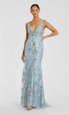A woman stands against a plain background wearing the Mac Duggal 67481, a sleeveless long floral-print formal dress in light blue with a deep V-neckline.