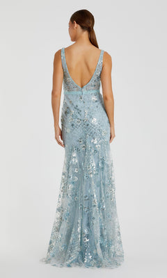 A woman faces away, wearing the Mac Duggal 67481 long formal dress—a sleeveless, floor-length gown in light blue with silver floral print and a deep V-back.