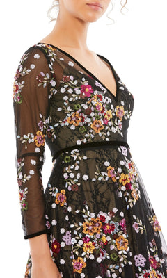 A woman wears the Mac Duggal 67499 Print Midi Wedding-Guest Dress, featuring sheer sleeves and colorful floral embroidery—shown from shoulders to mid-thigh, facing left—a stunning choice for any special occasion.