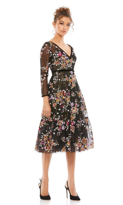 A woman in the Mac Duggal 67499 Print Midi Wedding-Guest Dress with black floral print, colorful embroidery, long sheer sleeves, and black heels stands against a white background.