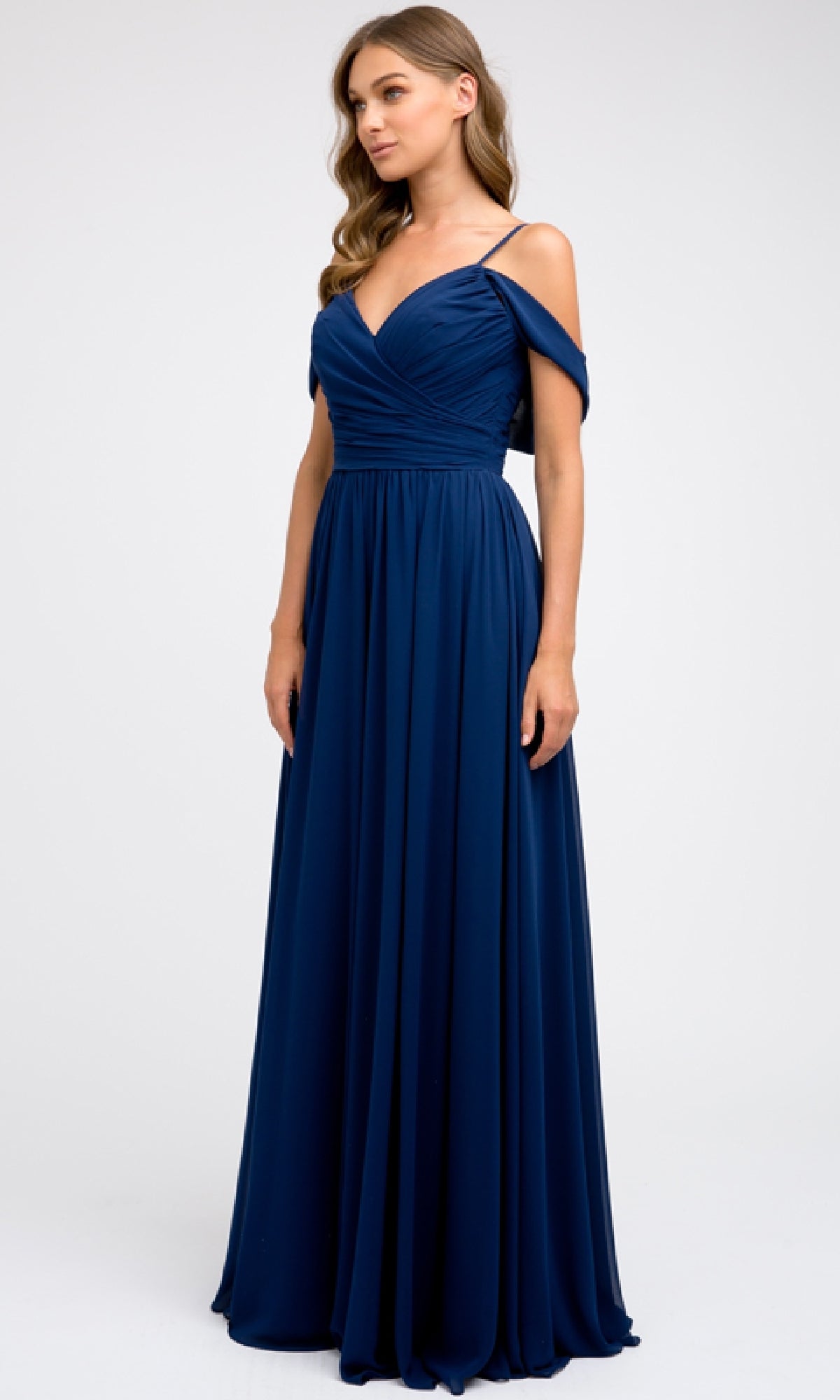 A woman models the Juliet 676 long prom dress—navy blue chiffon with off-the-shoulder straps, a fitted bodice, and an elegant A-line skirt—standing against a plain light background.