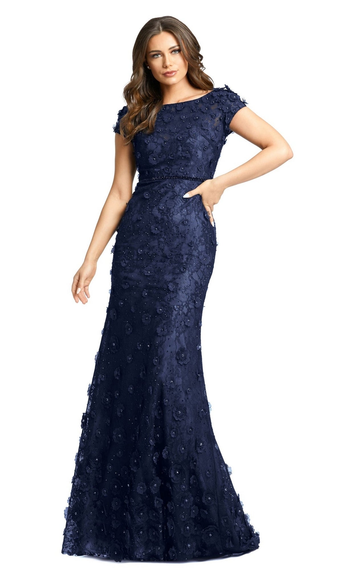 A woman poses against a white background in the Long Formal Dress 67711 by Mac Duggal, a lace fitted gown with short sleeves, navy blue floral appliqué details, and a floor-length silhouette.