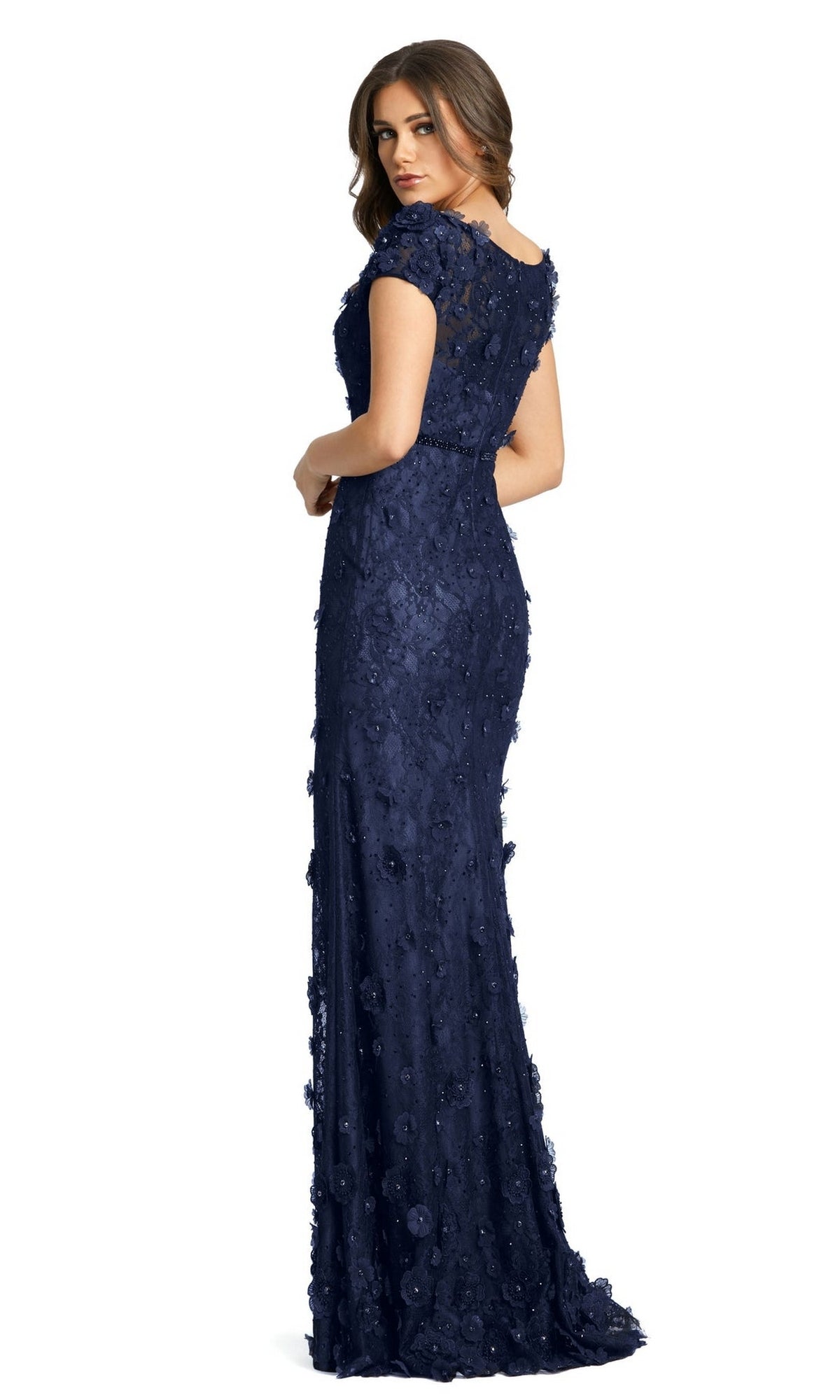 A woman models the Long Formal Dress 67711 by Mac Duggal—a navy blue, floor-length lace fitted gown with short sleeves—standing with her back turned and looking over her shoulder against a white background.