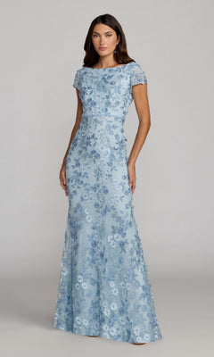 A woman poses in the Long Formal Dress 67711 by Mac Duggal—a fitted, light blue gown with short sleeves and delicate floral embroidery—against a plain background.