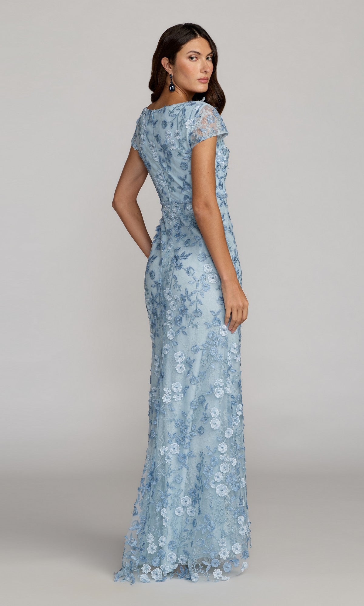 Woman in Mac Duggal Long Formal Dress 67711, a light blue floor-length lace gown with floral patterns and delicate applique, seen from the back against a neutral background.