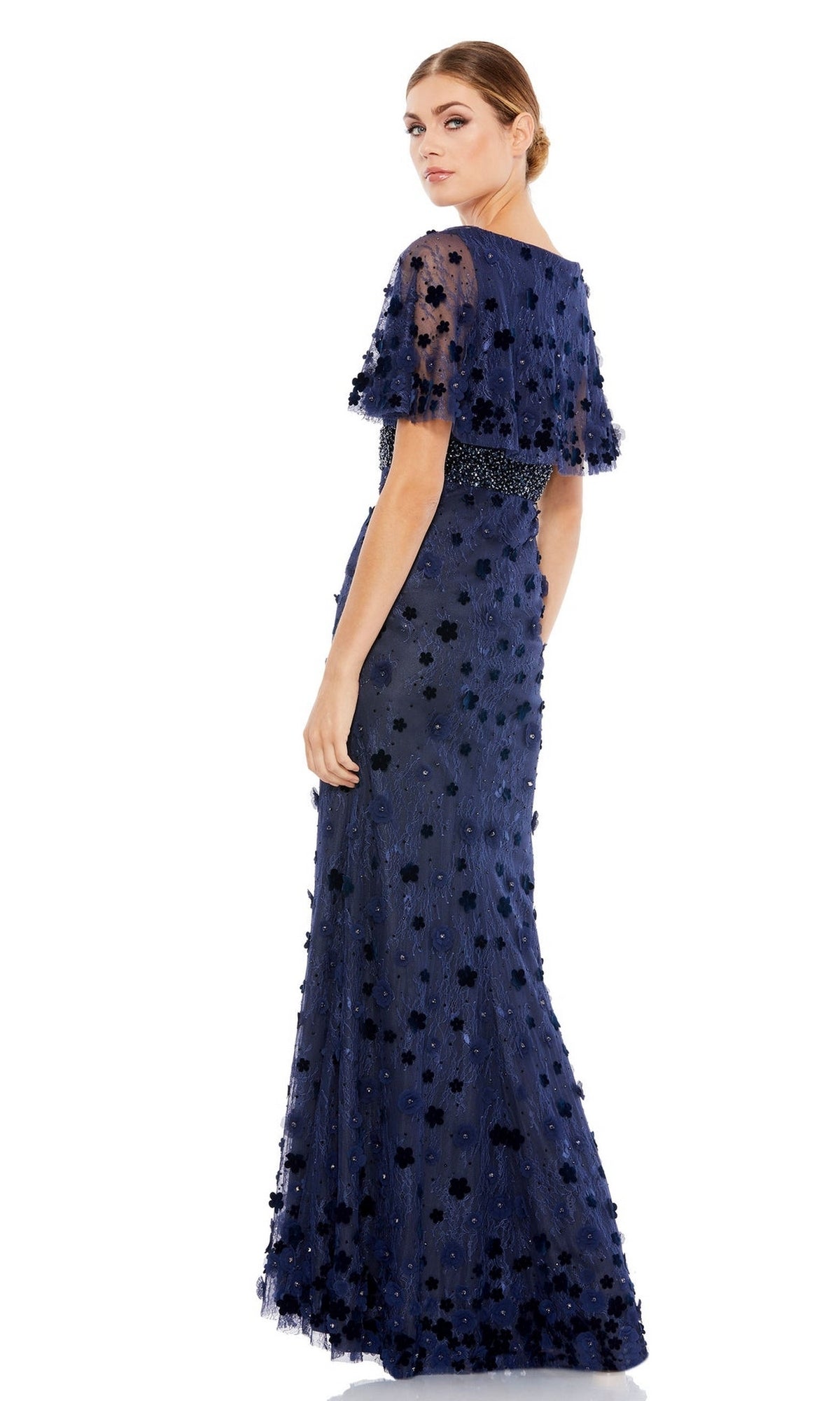 A woman stands looking over her shoulder in the Mac Duggal 67712, a navy blue long formal dress featuring short sheer sleeves and floral appliqué details.